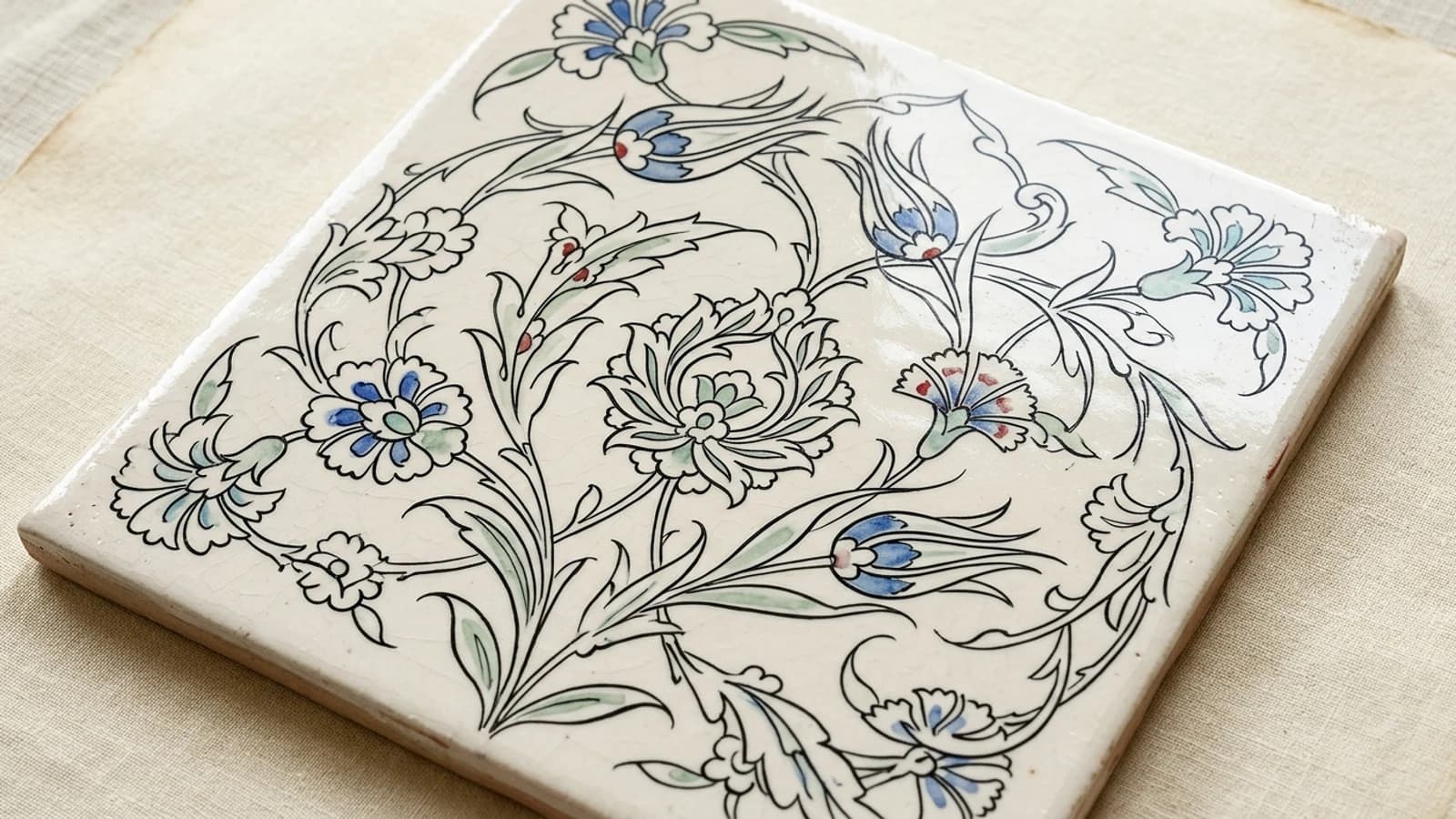 Illustration: a cream-glazed tile drawn almost entirely in fine black outline, with only a few carnations and tulip buds filled in blue and green.